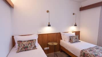 Ein Hotelzimmer mit zwei Betten, jeweils mit floraler Bettwäsche, einem kleinen runden Tisch und Wandlampen.