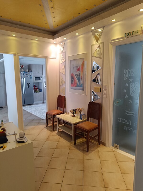 A modern interior with a dining area featuring two wooden chairs and a table, a kitchen in the background, and an exit sign above a door. - Skakkos Nafs Apartment with Wi-Fi in Nafpaktos (Ναύπακτος)