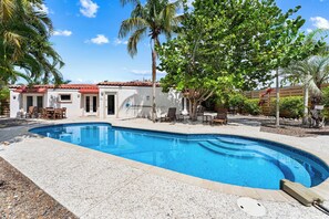 Ein Pool mit geschwungener Kante, umgeben von einer Terrasse mit Gartenmöbeln.