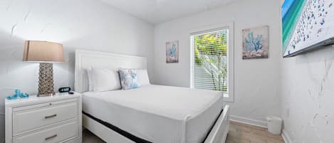 A bedroom with a white bed, a nightstand with a lamp, and artwork on the walls.