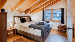 Ein Schlafzimmer mit Holzboden, einem Bett mit grauer Decke, einem Nachttisch mit Lampe und einem Fenster mit Vorhängen.