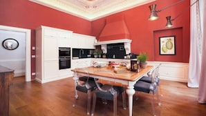 A kitchen with white cabinets, a wooden dining table, and a red accent wall. - GRAND FLORENTINE APARTMENT WITH FRESCOED CEILINGS NEAR THE UFFIZI (Firenze)