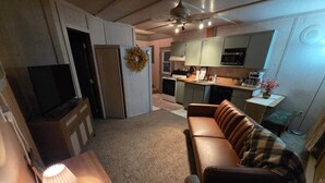 A compact living space with a kitchenette, a sofa, a table with a lamp, and a television. - The Nelson 2, Winner (Winner)