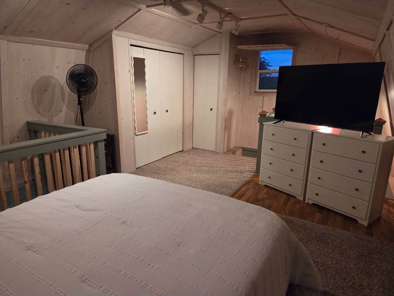 A bedroom with a bed, a dresser, a television, and a fan.