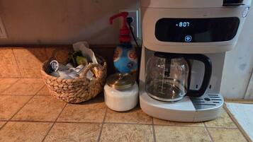 A coffee maker on a kitchen counter with a basket of items and a bottle of dish soap.