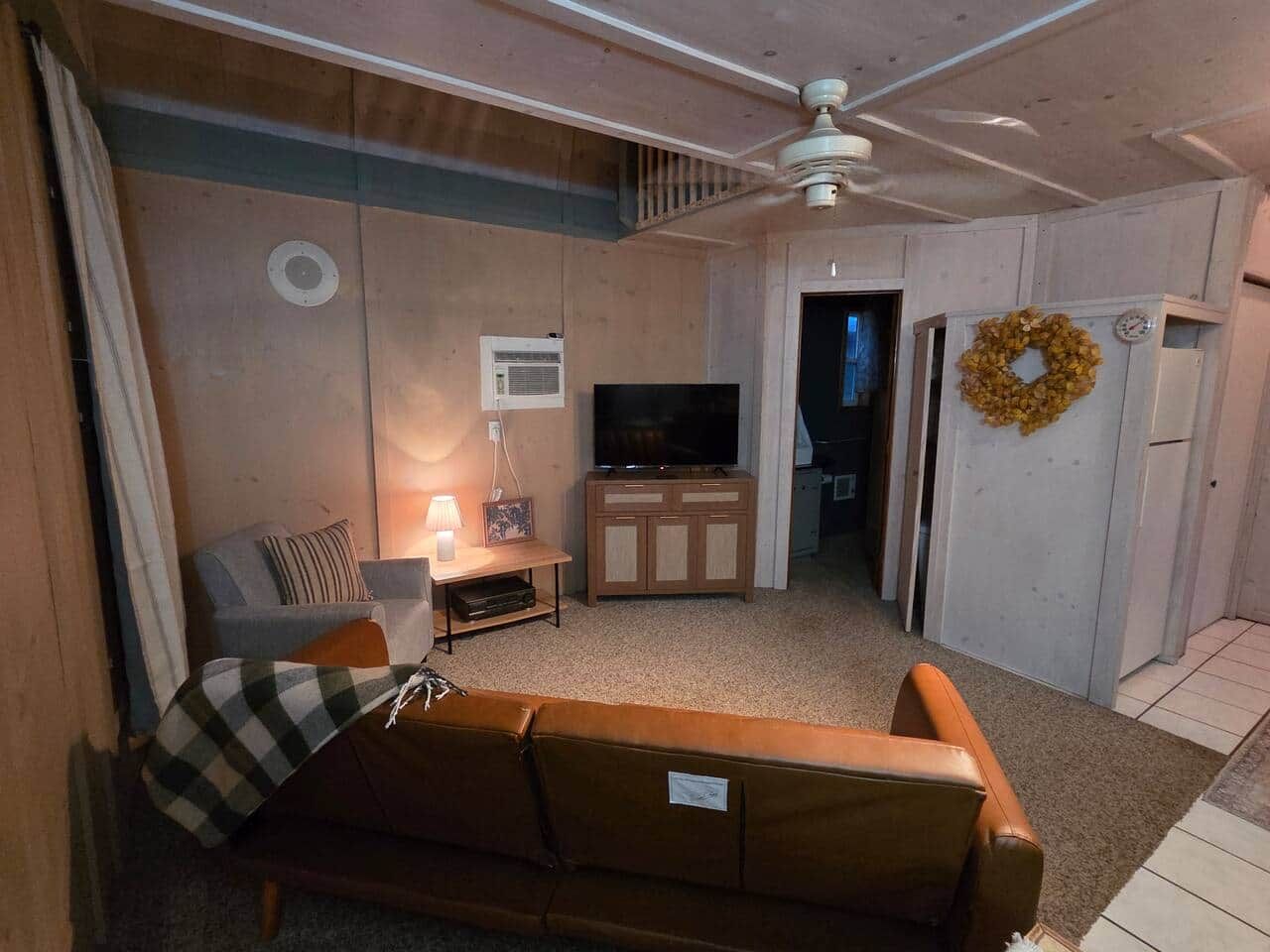 A compact living space with a sofa, a television, a ceiling fan, and a wall-mounted wreath.