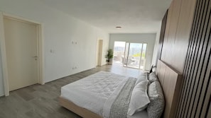Et soveværelse med en stor seng, et træhovedgærde, en skydedør til en balkon og udsigt til bygninger.