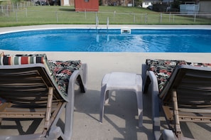 Ein Schwimmbecken mit Sprungbrett und Liegestühlen mit floralen Kissen.