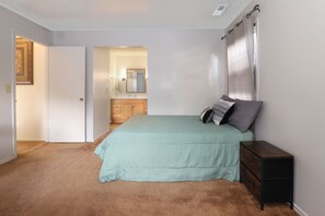 Un dormitorio con cama, mesita de noche, cómoda y puerta que da a otra habitación.