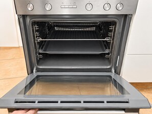 An open oven with two racks inside, a control panel with buttons and dials, and a tiled floor. - Vienna Escape 1BR Near Wiener Stadthalle (Wien)