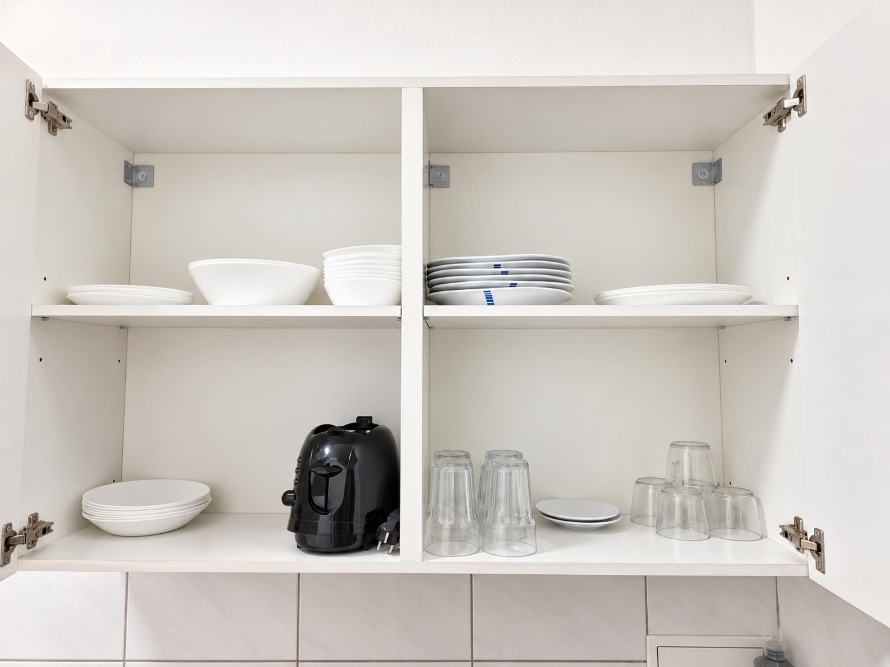 Een keuken met witte kasten, een koffiezetapparaat en glazen op de planken.