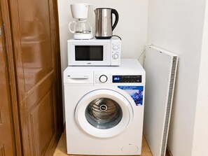 A compact laundry area with a washing machine, a microwave, and a coffee maker. - Vienna Escape 1BR Near Wiener Stadthalle (Wien)