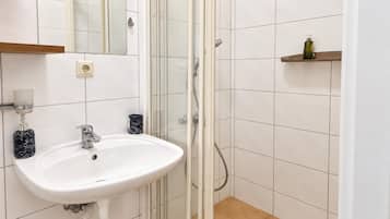 A bathroom with a white sink, a glass shower enclosure, and a beige floor.