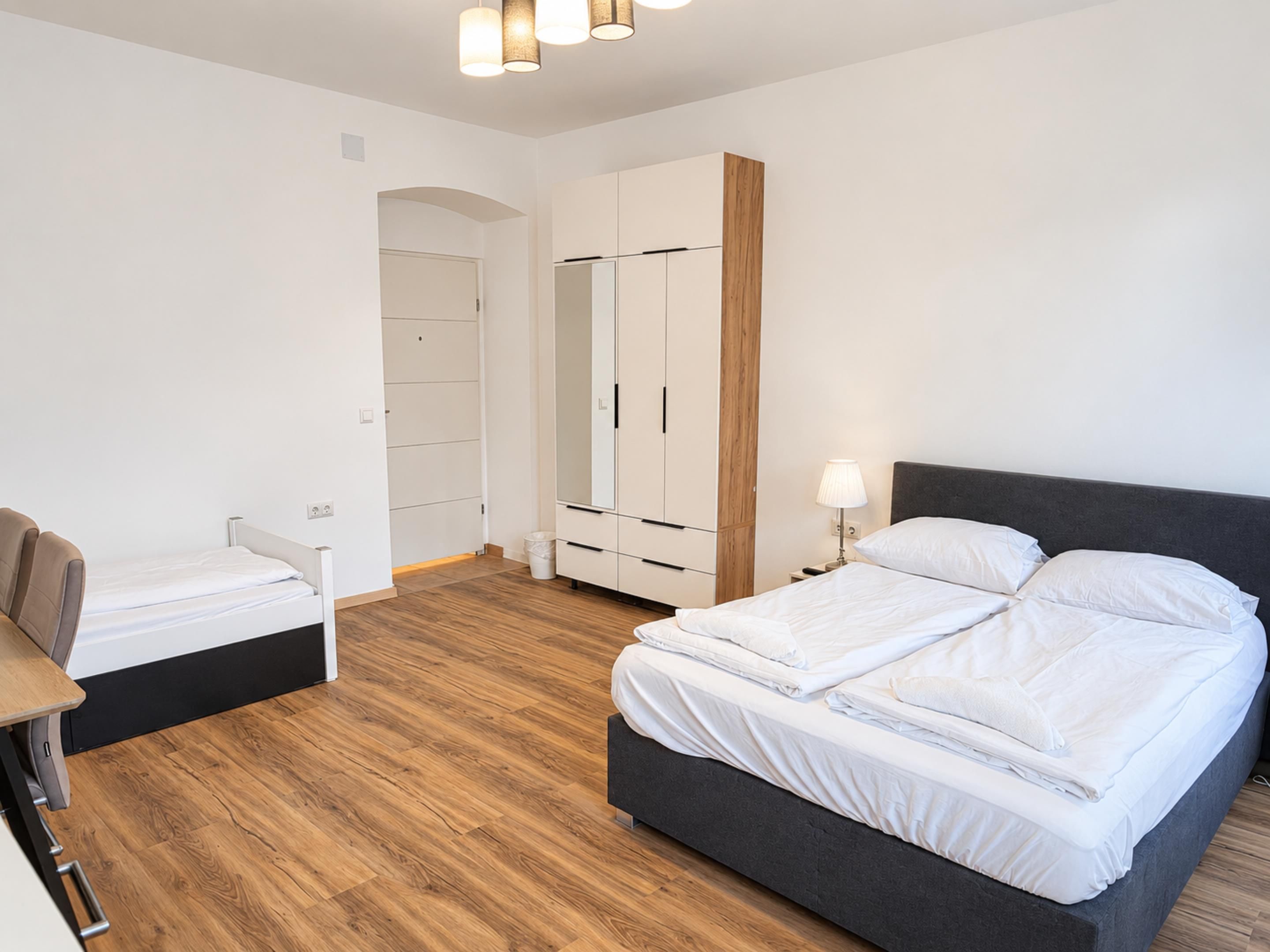 Un dormitorio moderno con cama, mesita de noche, armario y escritorio con silla.