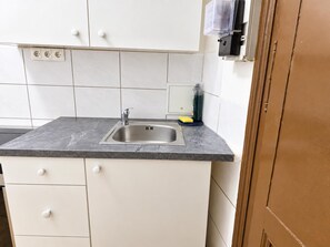 A kitchen with a stainless steel sink, white cabinets, and a grey countertop. - Vienna Escape 1BR Near Wiener Stadthalle (Wien)