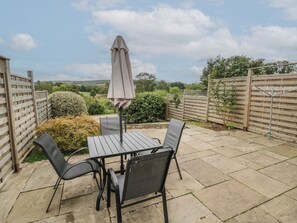 An outdoor patio with a table and chairs, surrounded by wooden fences and greenery. - Russet Bungalow (Worcester)