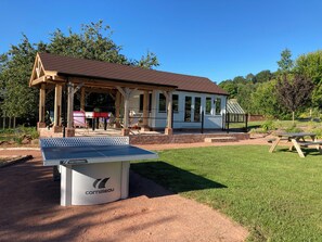 A covered pavilion with a table tennis table in front, surrounded by a grassy area and trees. - Russet Bungalow (Worcester)