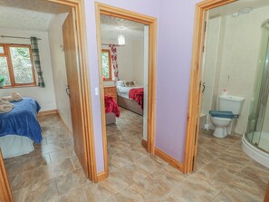 A room with a bed, a bathroom with a toilet and shower, and a hallway leading to another room. - Russet Bungalow (Worcester)