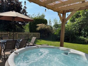 A hot tub under a wooden pergola with a table and chairs nearby. - Chaff House (Worcester)