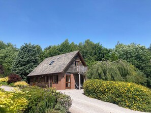A log cabin with a sloped roof, a balcony, and surrounded by a garden with yellow flowers. - Heron Lodge (Worcester)