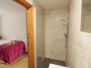 A bathroom with a shower, a bed with a pink blanket, and a wooden door frame. - Heron Lodge (Worcester)