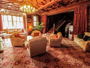 A spacious living room with a grand staircase, multiple armchairs, and a piano. - Rochester Apartment (Penrith)