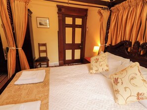 Ein Hotelzimmer mit einem Bett, Vorhängen, einer Holztür, einem Stuhl und einer Lampe.