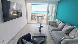 Una sala de estar moderna con una televisión de pantalla plana, un sofá, una mesa de centro y vistas al exterior a través de un ventanal corredero.