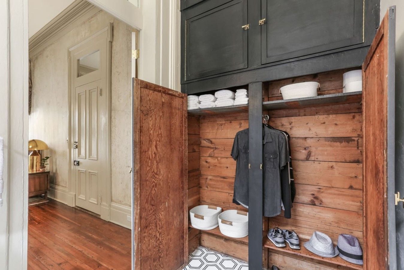 Ein Holzschrank mit Regalen, einer Kleiderstange und einer Tür zu einem anderen Raum.