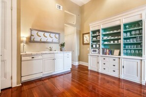 A kitchen with white cabinetry, a wooden floor, and a green glass display cabinet. - Casabianca: Elegant Flat in Historic Magazine Row (New Orleans)