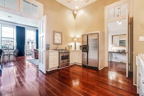 A kitchen with wooden flooring, white cabinets, a stainless steel refrigerator, and a dining area with a table and chairs. - Casabianca: Elegant Flat in Historic Magazine Row (New Orleans)