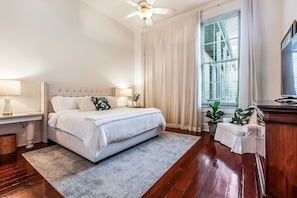 A bedroom with a bed, bedside tables, a ceiling fan, a window with blinds, and a television. - Casabianca: Elegant Flat in Historic Magazine Row (New Orleans)