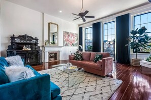 A spacious living room with a blue sofa, a pink sofa, a glass coffee table, and a fireplace. - Casabianca: Elegant Flat in Historic Magazine Row (New Orleans)