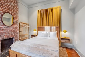 A hotel room with a brick fireplace, a large bed with white bedding, a wooden headboard, and two bedside lamps. - Vibrant 3BR/3BA St Charles Ave Apt w/ Balcony (New Orleans)