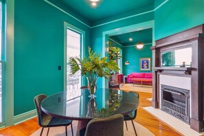 Une pièce aux murs de couleur turquoise, avec une table en verre, des chaises, un canapé rose et une cheminée.
