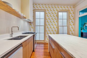 A modern kitchen with a wooden countertop, stainless steel sink, and a window with a banana pattern wall. - Vibrant 3BR/3BA St Charles Ave Apt w/ Balcony (New Orleans)