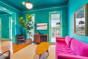A room with teal walls, a pink sofa, a wooden coffee table, a potted plant, and a framed picture on the wall. - Vibrant 3BR/3BA St Charles Ave Apt w/ Balcony (New Orleans)