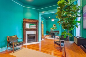 A room with teal walls, a fireplace, wooden flooring, and a dining area with a table and chairs. - Vibrant 3BR/3BA St Charles Ave Apt w/ Balcony (New Orleans)