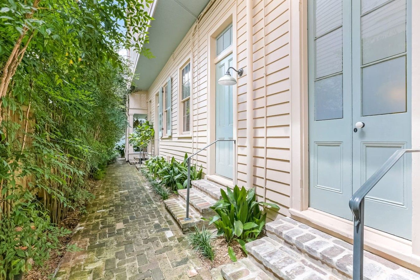 A narrow stone pathway leading to a building with a light-colored exterior and blue shutters.
