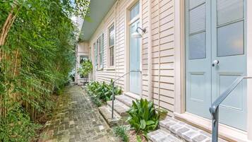 A narrow stone pathway leading to a building with a light-colored exterior and blue shutters.