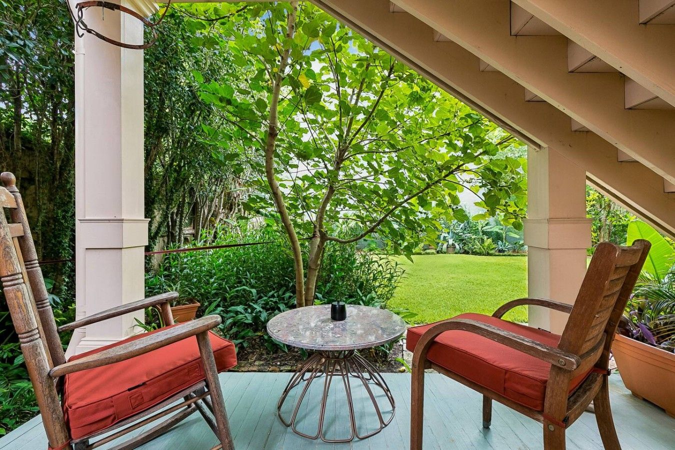 An outdoor patio with a round table and two wooden chairs with red cushions.