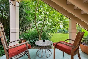 Een terras buiten met een ronde tafel en twee houten stoelen met rode kussens.