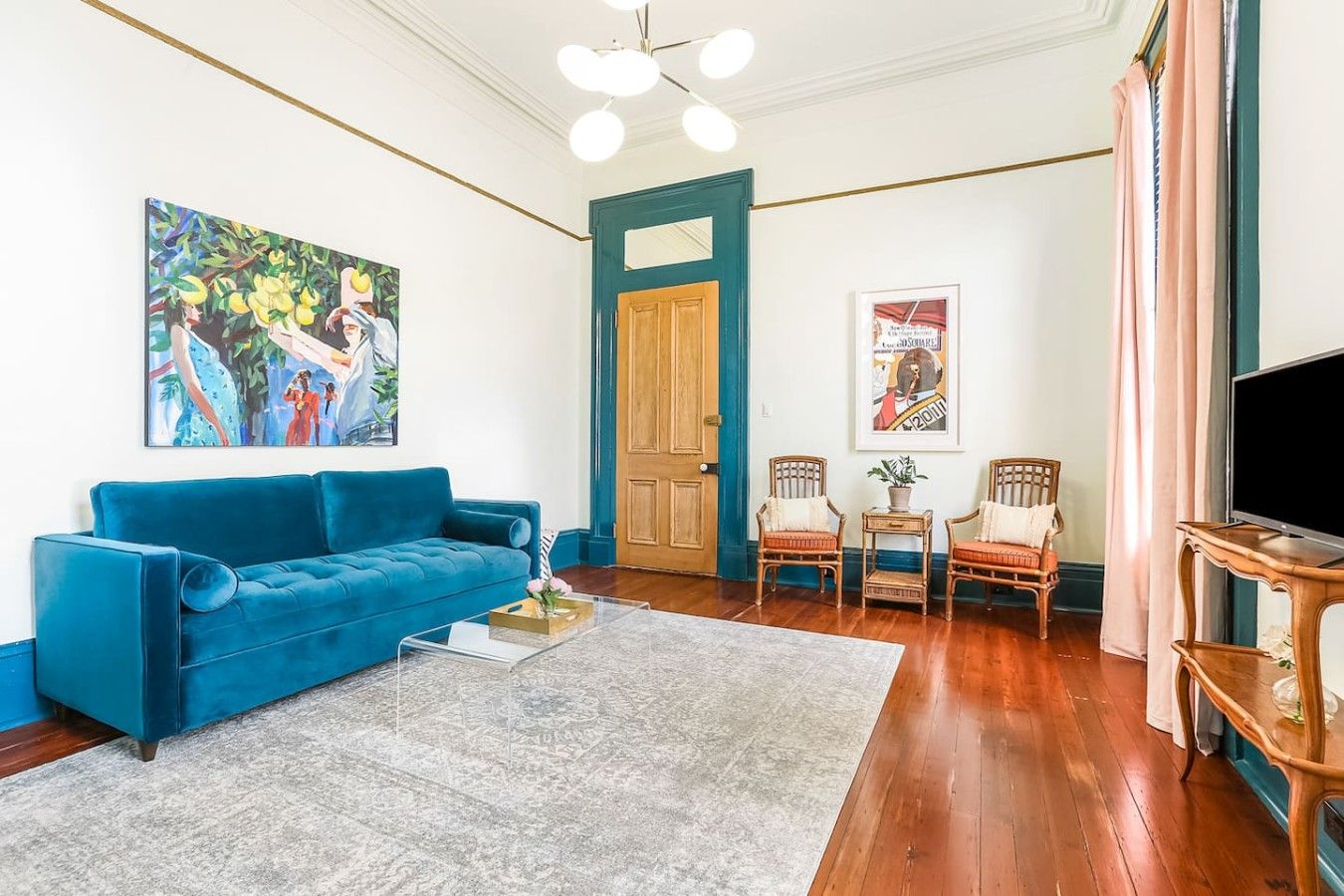 A living room with a blue sofa, a coffee table, a painting, a door, and a television.