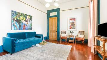 A living room with a blue sofa, a coffee table, a painting, a door, and a television.