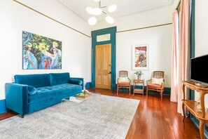 Een woonkamer met een blauwe bank, een salontafel, een schilderij, een deur en een televisie.