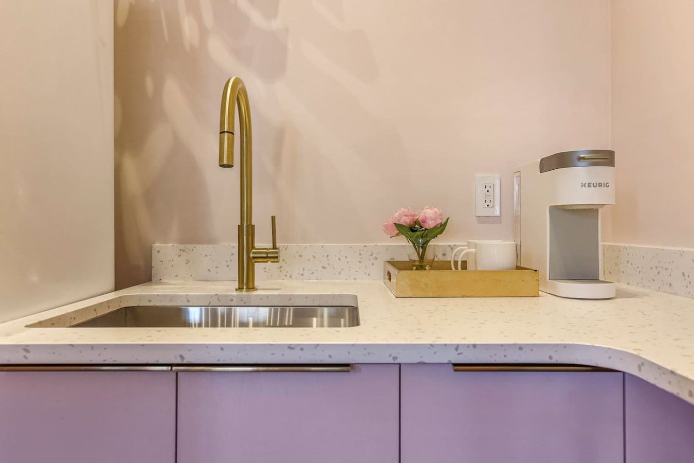 Eine Küche mit einem goldenen Wasserhahn, einer Kaffeemaschine und einer Vase mit Blumen auf der Arbeitsfläche.