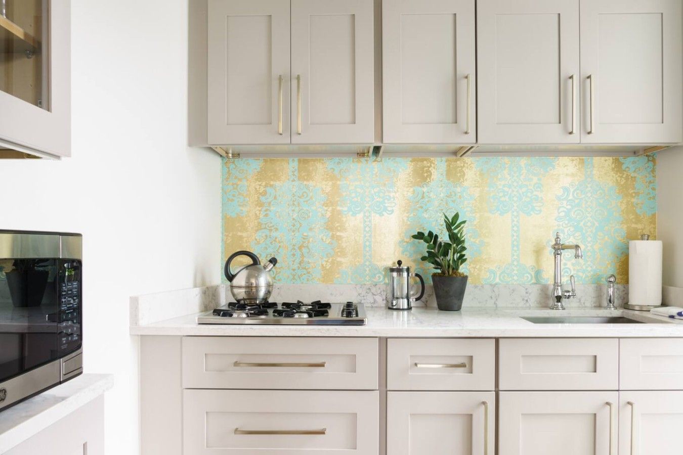 A kitchen with white cabinets, a gas stove, a kettle, a coffee pot, and a sink.