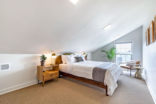 Een slaapkamer met een bed, nachtkastjes, een lamp, een stoel en een raam.
