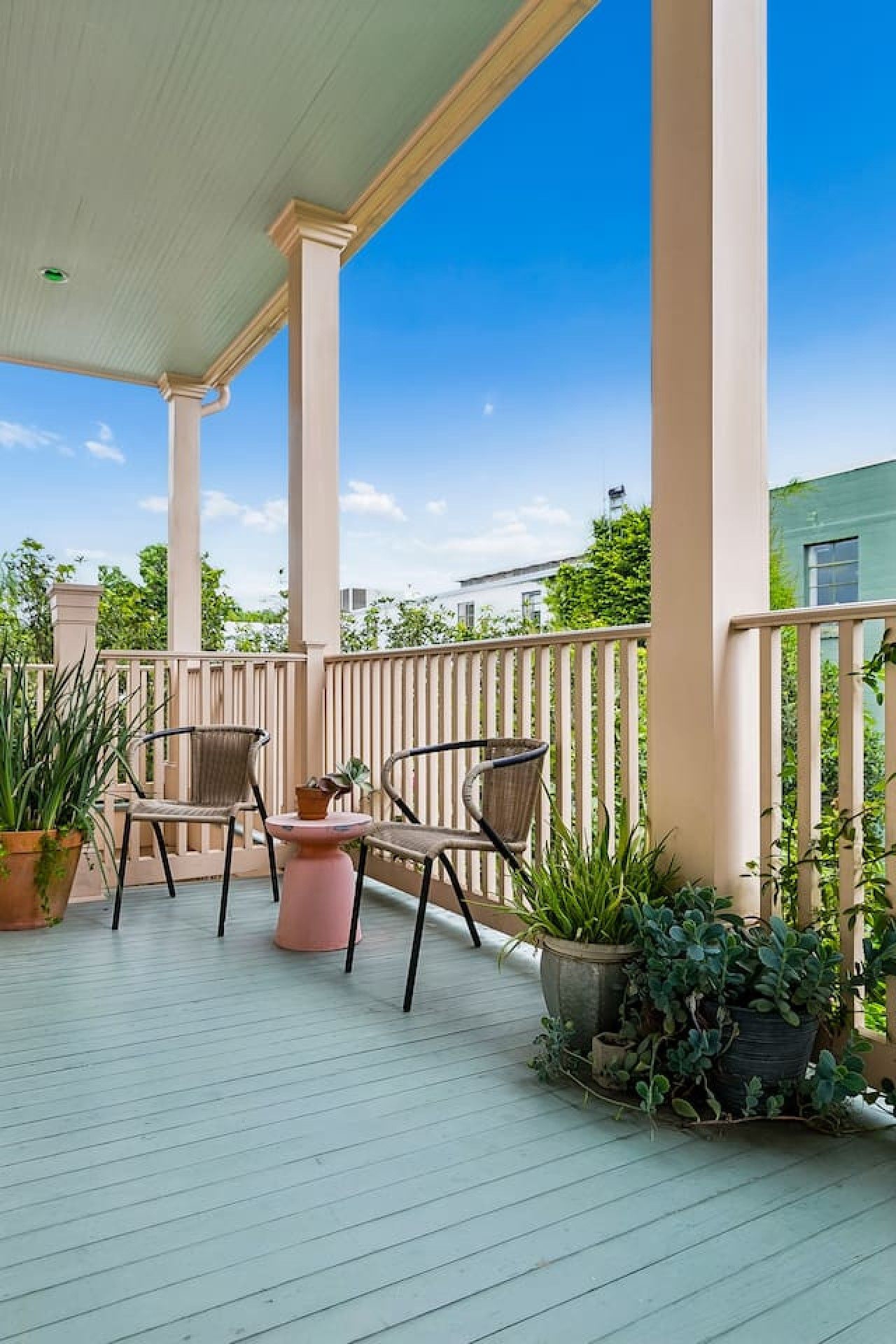 A covered outdoor area with a wooden deck, two wicker chairs, a small round table, and potted plants.