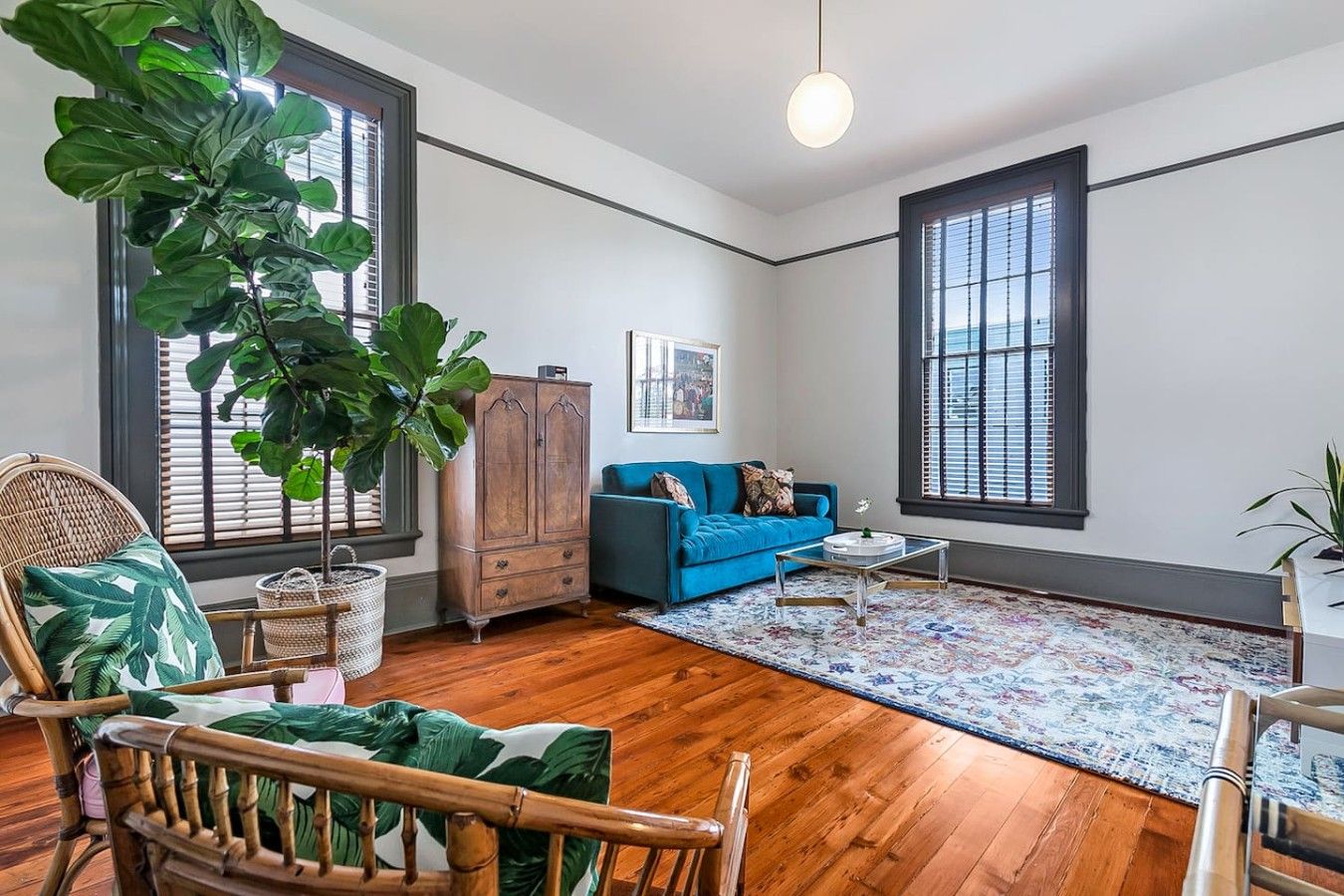 A living room with a blue sofa, a wooden cabinet, a large green plant, and a wicker chair.